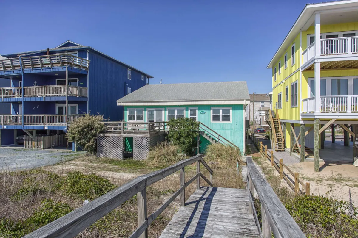 A charming exterior scene featuring colorful houses, a welcoming wooden walkway, and lush greenery. The mood is cheerful, hinting at gatherings and relaxing evenings after exploring the town.