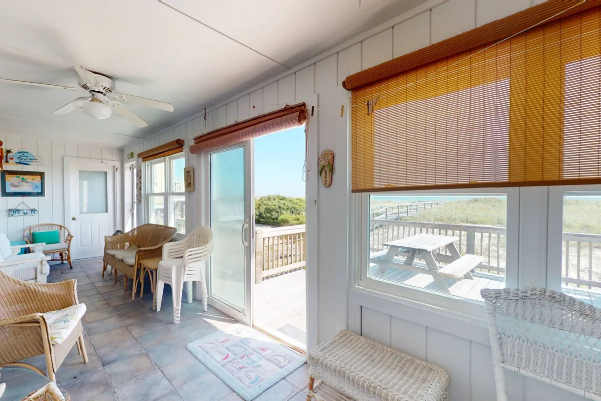 This image captures the interior seating area with large windows framing an outdoor picnic table and expansive ocean views beyond. It conveys the seamless connection between indoor comfort and the outdoor deck experience, inviting guests to relax with a book or gather for social time while still enjoying the oceanfront scenery.