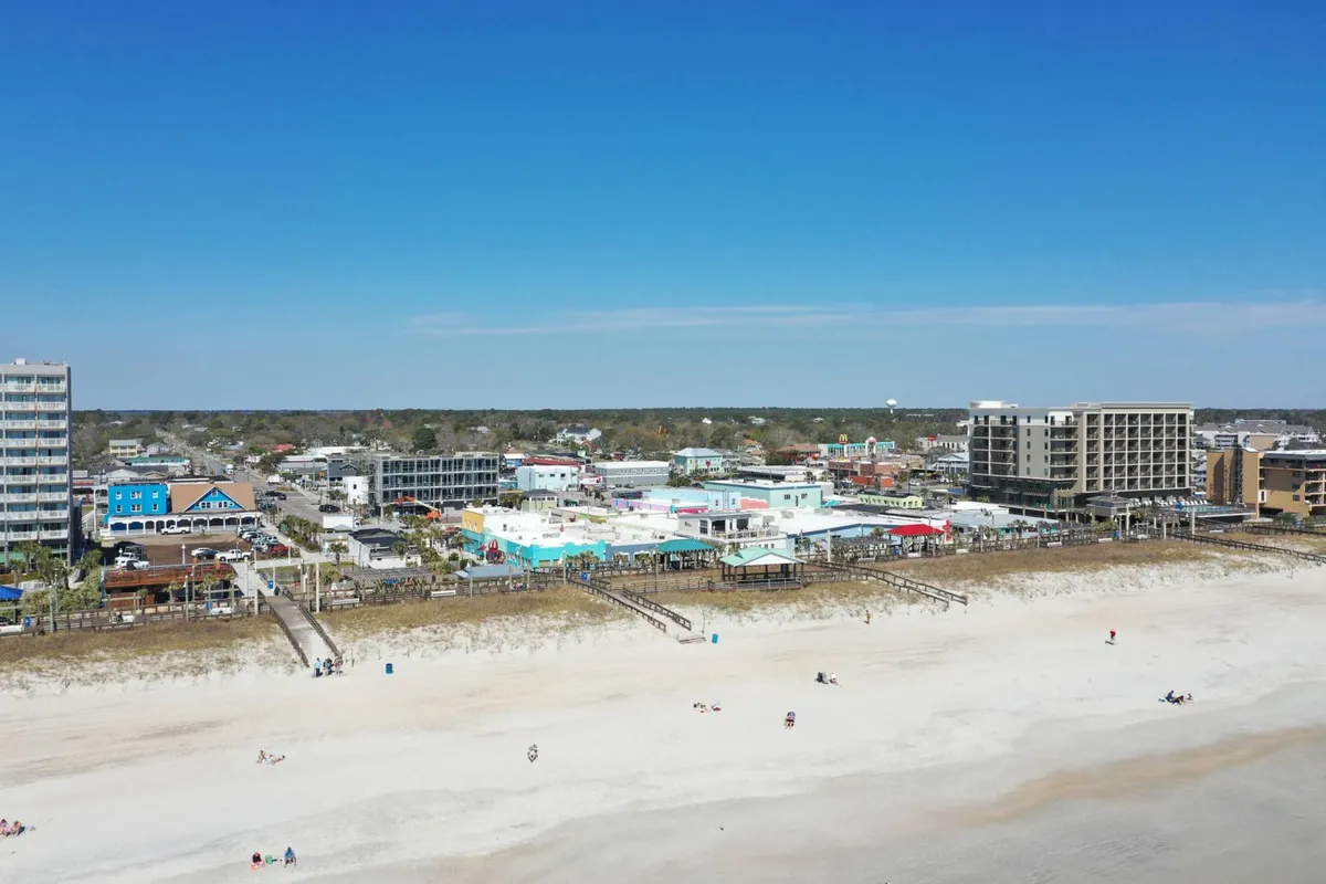 A lively view of the Carolina Beach boardwalk, with colorful buildings lighting up the evening, people enjoying their time on the beach, and the energy of local shops and restaurants. The boardwalk is bustling, suggesting a vibrant scene perfect for nightlife, festivals, and community events.