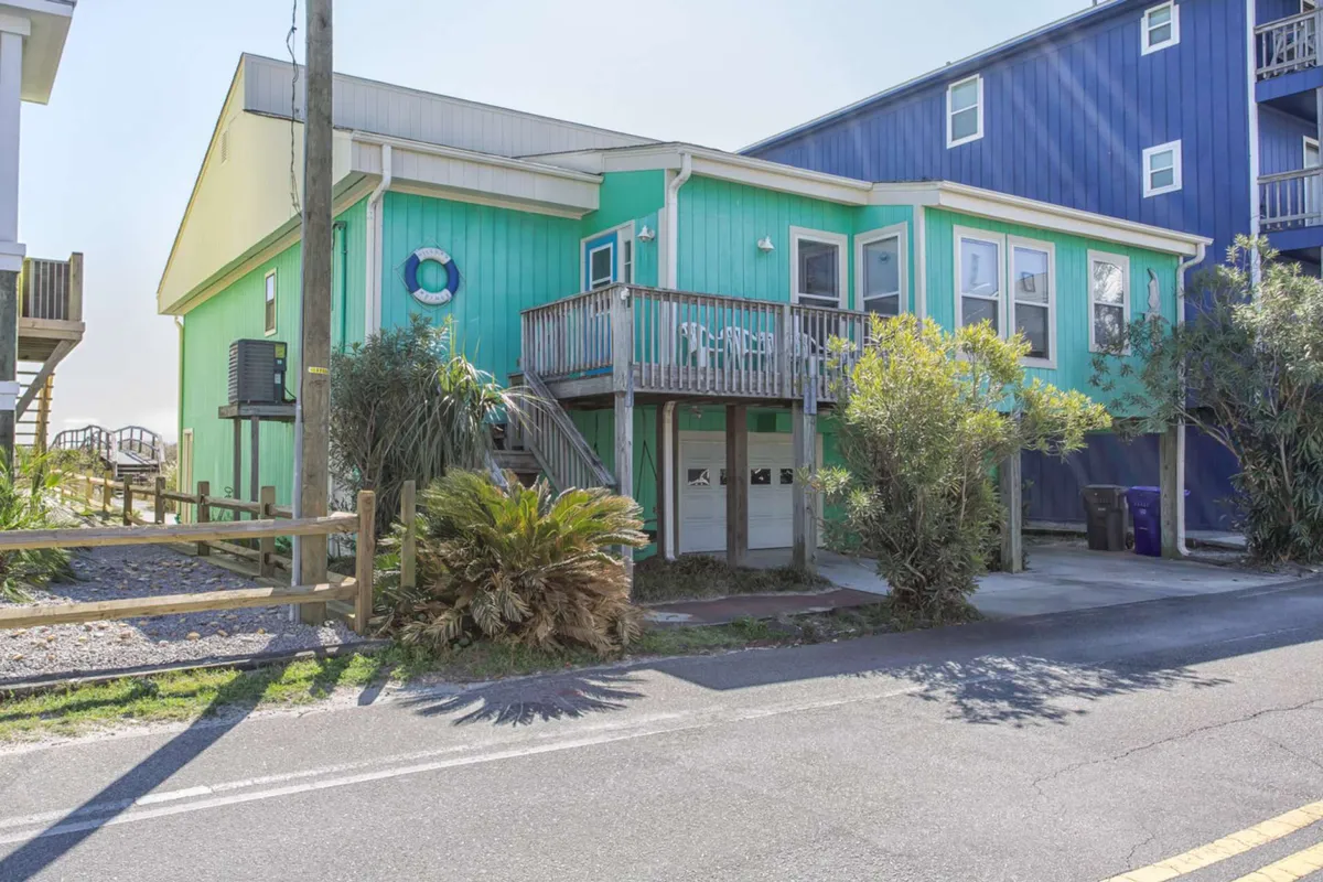 The brightly colored exterior of a beach cottage is framed by palm trees and a wooden balcony. The cheerful façade invites you to relax outdoors, whether sipping morning coffee or winding down after a day of boardwalk adventures.